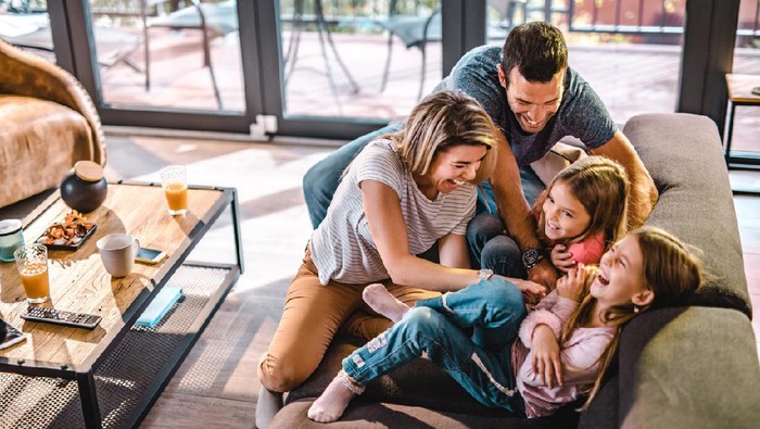 High angle view of cheerful parents having fun while tickling their daughters on sofa in the living room.