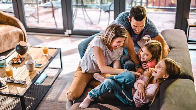 High angle view of cheerful parents having fun while tickling their daughters on sofa in the living room.