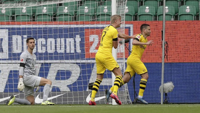 Dortmund's Raphael Guerreiro, right, celebrates after scoring the opening goal past Wolfsburg's goalkeeper Koen Casteels, left, during the German Bundesliga soccer match between VfL Wolfsburg and Borussia Dortmund in Wolfsburg, Germany, Saturday, May 23, 2020. The German Bundesliga is the world's first major soccer league to resume after a two-month suspension because of the coronavirus pandemic. (AP Photo/Michael Sohn, Pool)