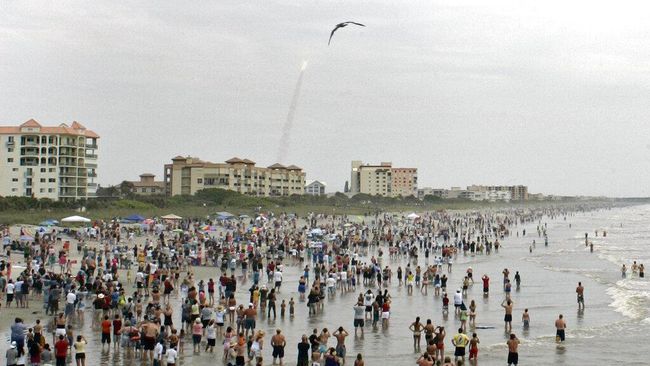 FILE - In this Friday, July 8, 2011 file photo, crowds gather in the surf and on the beach in Cocoa Beach, Fla., to watch the launch of the space shuttle Atlantis on STS-135. This is the final U.S. shuttle mission before the fleet is retired. In ordinary times, the beaches and roads along Florida’s Space Coast would be packed with hundreds of thousands of spectators, eager to witness the first astronaut launch from Florida in nine years, scheduled for May 27, 2020. In the age of coronavirus, local officials and NASA are split on whether that's a good idea. (AP Photo/Dave Martin)