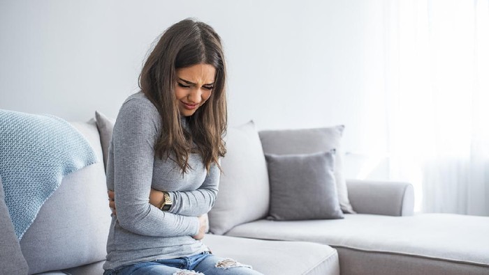 Woman lying on sofa looking sick in the living room. Beautiful young woman lying on bed and holding hands on her stomach. Woman having painful stomachache on bed, Menstrual period