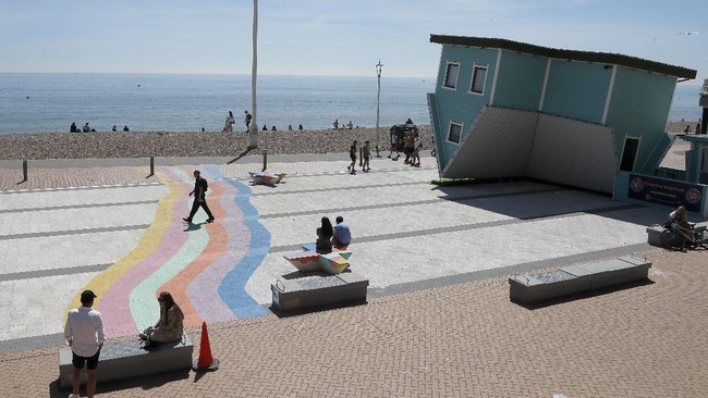 People walk by the upside down house on the beach in Brighton, England, Wednesday, May 20, 2020. Lockdown restrictions due to the coronavirus outbreak have been relaxed allowing unlimited outdoor exercise and activities such as sunbathing. (AP Photo/Frank Augstein)