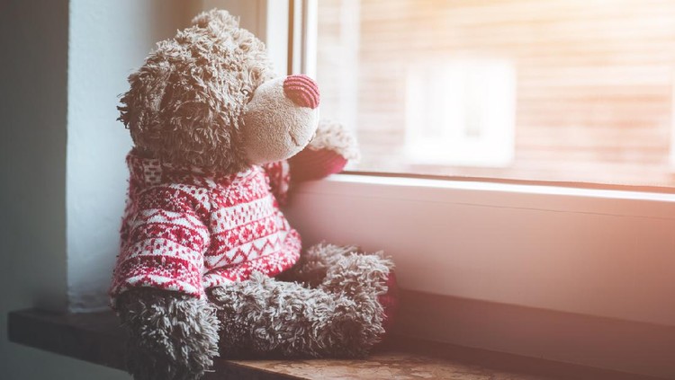 Cute teddy bear is sitting on the windowsill, looking out of the window