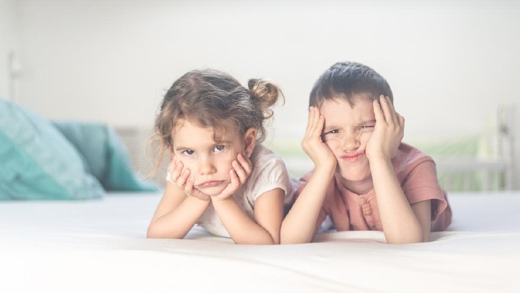 Beautiful brother and sister are lying down in bedroom and having so much fun smiling and making silly faces.