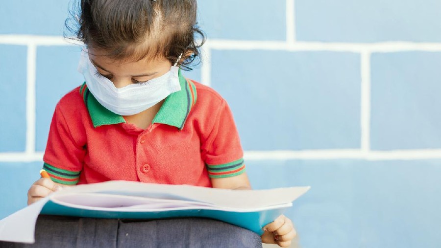 Anak sekolah Covid 19 or Coronavirus and Air pollution pm2.5 concept - Little girl wearing medical mask and busy in writing at school - showing Wuhan covid-19 or sars cov 19 outbreak or epidemic of virus