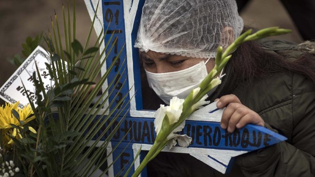 Katherine Huallpatuero embraces a cross while mourning the death of her father Romulo Huallpatuero, 50 , who died from COVID-19, at the Nueva Esperanza cemetery on the outskirts of Lima, Peru, Tuesday, May 26, 2020. (AP Photo/Rodrigo Abd)