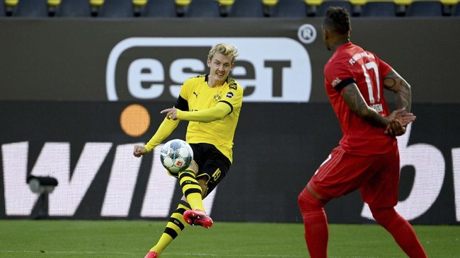 Dortmund's Julian Brandt, left, plays the ball past Munich's Jerome Boateng, right, during the German Bundesliga soccer match between Borussia Dortmund and FC Bayern Munich in Dortmund, Germany, Tuesday, May 26, 2020. The German Bundesliga is the world's first major soccer league to resume after a two-month suspension because of the coronavirus pandemic. (Federico Gambarini/DPA via AP, Pool)