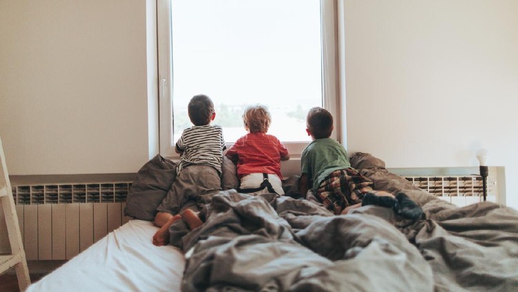 Photo of a curious little boys, looking out of a window from their bedroom