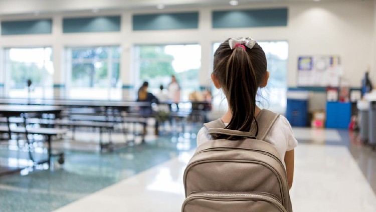 Elementary schoolgirl enters the school cafeteria. She pauses while looking for a friend.