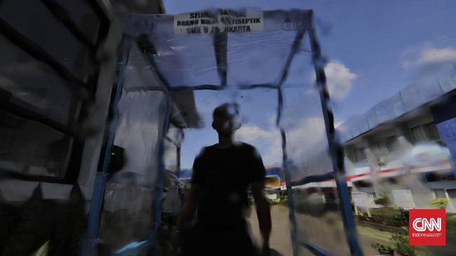 Staf SMKN 26 Rawamangun, Jakarta Timur, menggunakan ruang disinfektan kreasi sekolah itu yang menggunakan sensor gerak dan tenaga surya dalam rangka pelayanan penerimaan peserta didik baru (PPDB) 2020 dengan standar pencegahan penyebaran pandemi Covid-19,  Sabtu, 30 Mei 2020. Persiapan ini dilakukan SMKN 26 Rawamangun  yang ditunjuk sebagai posko PPDB untuk melayani peserta penerimaan calon peserta didik sejumlah sekolah di area Timur I. CNN Indonesia/Adhi Wicaksono