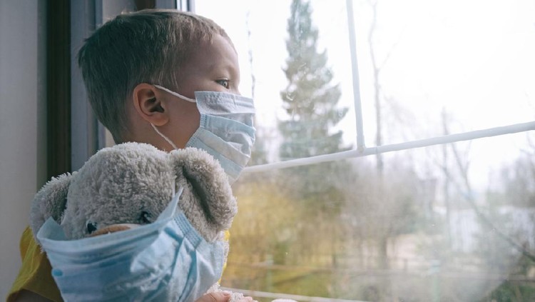Sad illness child on home quarantine. Boy and his teddy bear both in protective medical masks sits on windowsill and looks out window. Virus protection, coronavirus pandemic, prevention epidemic.