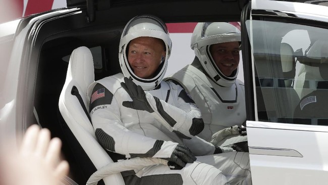 NASA astronauts Douglas Hurley, left, and Robert Behnken wave while seated in a Tesla SUV on their way to Pad 39-A, at the Kennedy Space Center in Cape Canaveral, Fla., Saturday, May 30, 2020. The two astronauts will fly on a SpaceX test flight to the International Space Station. For the first time in nearly a decade, astronauts will blast into orbit aboard an American rocket from American soil, a first for a private company. (AP Photo/John Raoux)