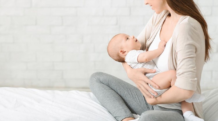 Closeup of young woman holding cute little baby in her hands, lulling him in bed. Panorama with free space