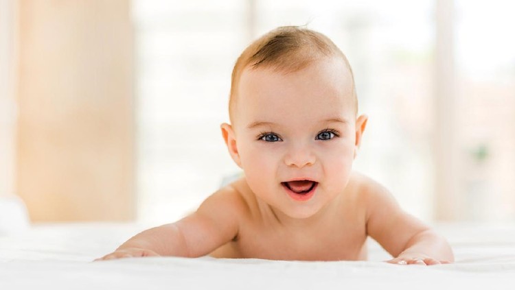 Portrait of happy baby boy lying down in bed and looking at camera.