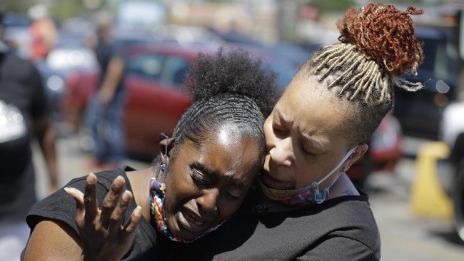 Two women pray, Tuesday, June 2, 2020, in Louisville, Ky., near the intersection where David McAtee was killed Sunday evening. Louisville police say video obtained from security cameras at McAtee’s business and an adjoining business show that McAtee fired a gun as police and National Guard soldiers were enforcing a curfew approached his business. (AP Photo/Darron Cummings)