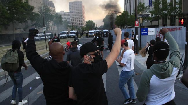 Protesters react in front of a police line as a barricade burns during a demonstration Tuesday, June 2, 2020 in Paris. Paris riot officers fired tear gas as scattered protesters threw projectiles and set fires at an unauthorized demonstration against police violence and racial injustice. Several thousand people rallied peacefully for two hours around the main Paris courthouse in homage to George Floyd and to Adama Traore, a French black man who died in police custody. (AP Photo/Michel Euler)