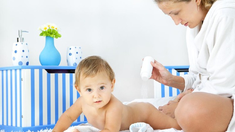 Mother pampering her baby girl daughter at home, applying baby powder to her body. Real people, mother 30-35, baby girl 10 months.