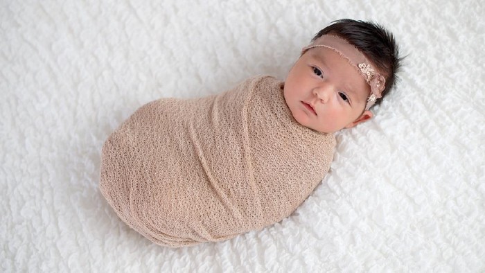 One month old baby girl swaddled in a beige wrap. Shot in the studio on a white blanket.