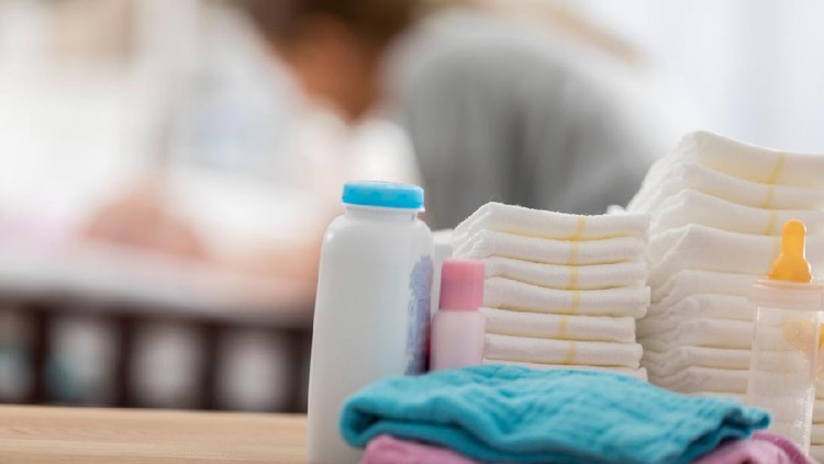 Close up of baby products sitting on a table in a baby's nursery. A mom is changing a baby's diaper in the background.