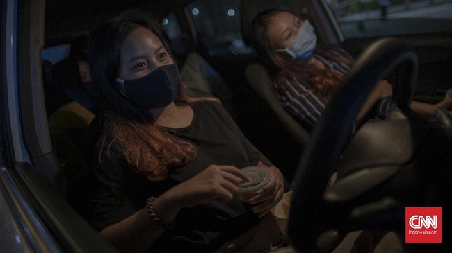Pemutaran film dan iklan layanan masyarakat pada layar videotron di lahan parkir salah satu pusat perbelanjaan di kawasan Cikarang, Bekasi, Jawa Barat, Selasa, 2 Juni 2020. Pemutaran film ini berfungsi sebagai hiburan ketika pengunjung menunggu pesanan makanan agar tidak terjadi penumpukan antrean di gerai makanan yang dituju, sehingga pengunjung bisa tetap menunggu di mobil sembari menyaksikan tayangan yang ditampilkan pada layar videotron dan juga sebagai upaya mendukung protokol kesehatan pemerintah terkait aturan jaga jarak sosial sebagai upaya memutus rantai penyebaran Covid-19. CNN Indonesia/Bisma Septalisma