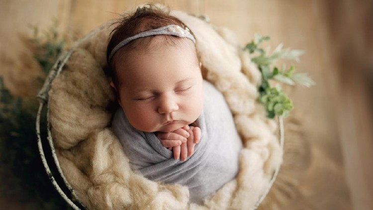 20 day old baby girl with chunky cheeks, swaddled in pale purple with a matching headband, in a prop basket for her newborn milestone photos
