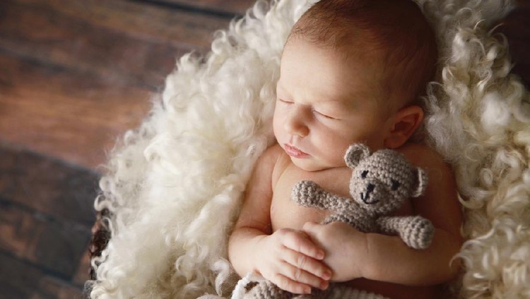 637355730 A beautiful newborn baby boy hugs a little teddy bear as he sleeps. He is lying on a soft blanket of curly wool.