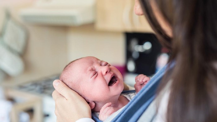 Close up of unrecognizable young mother with her crying newborn baby son in sling at home