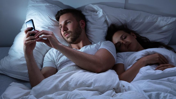 Young Man Using Cellphone While Her Wife Sitting On Bed At Night