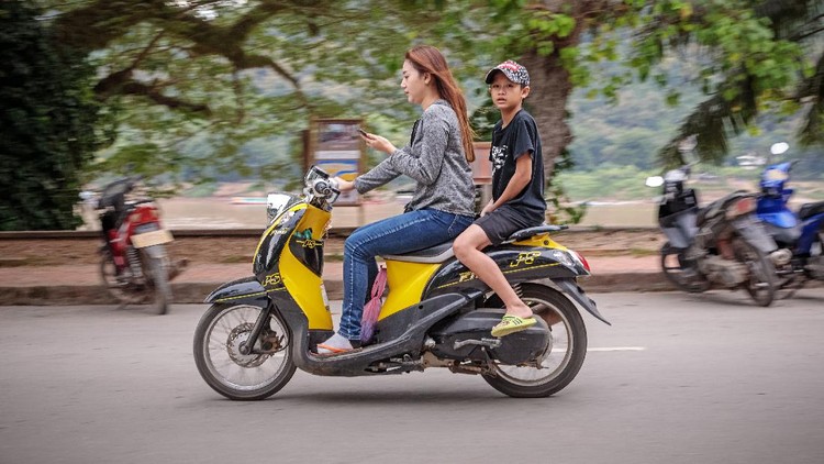 Khem Khong, Luang Prabang, Laos - December 11, 2018: Mother and son on a motorcycle in main street of the former capital of Laos