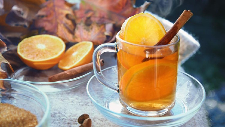 hot ginger tea with orange slices and cinnamon in a glass cup on a blanket and some red autumn leaves, selected focus, narrow depth of field