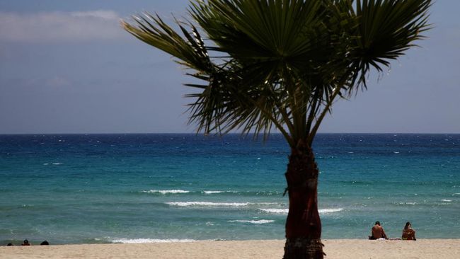 FILE - In this file image taken on Sunday, May 10 2020, sunbathers sit on an empty stretch of 'Landa' beach at the Cyprus seaside resort of Ayia Napa, a favorite among tourists.  Cyprus' government Wednesday May 27, 2020, is pledging to cover all costs for anyone testing positive for the coronavirus while on vacation in the east Mediterranean island nation, covering the costs of lodging, food, drink and medication for COVID-19 patients and their families.(AP Photo/Petros Karadjias, FILE)