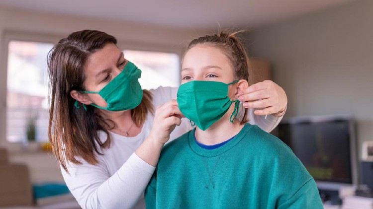 Mother wearing a green homemade protective face mask and putting one to her daughter at home during the coronavirus Covid-19.