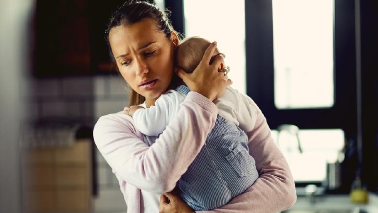 Young mother holding her baby son and consoling him at home.