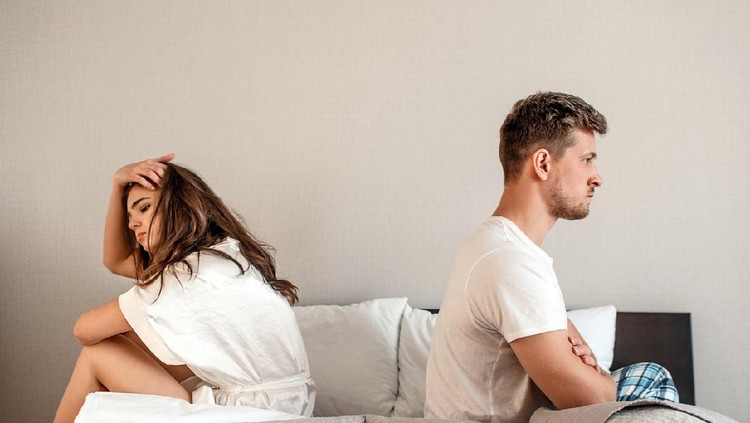 Young couple in the bedroom. Unhappy man and woman are sitting back to back in the bed, couple quarrel home scene, break in relations