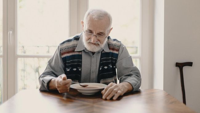 Sad lonely senior man eating soup in empty apartment