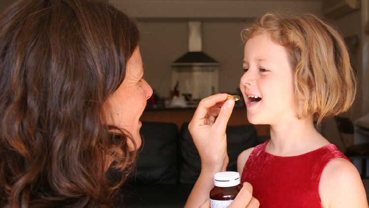 young girl being given childrens supplements or vitamin by her mother