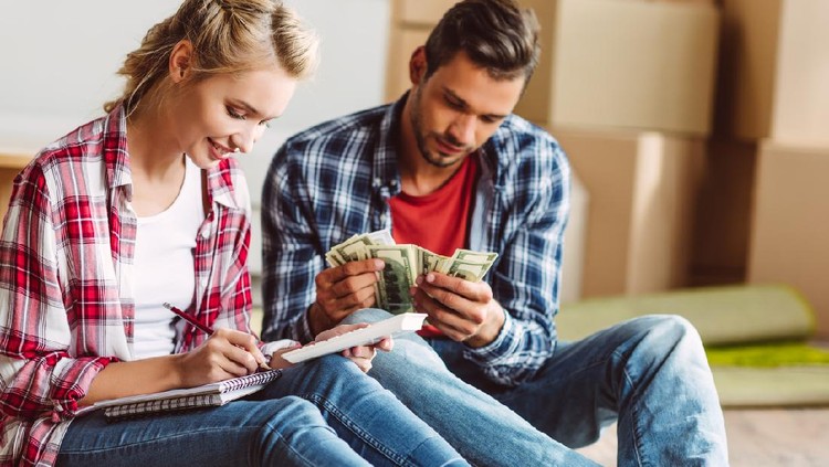 young couple counting money while sitting on floor in new apartment