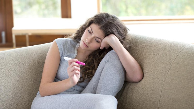 Young woman looking miserable staring at pregnancy test