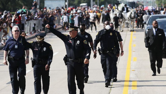 PEARLAND, TEXAS - JUNE 09: Houston Police Chief Art Acevedo (3rd L) and another police officer raise their hands while walking in front of the casket containing the remains of George Floyd as it is brought by horse-drawn carriage (TOP R) in a funeral procession to Houston Memorial Gardens Cemetery for burial, on June 9, 2020 in Pearland, Texas. George Floyd died on May 25th when he was in Minneapolis police custody, sparking nationwide protests. A white police officer, Derek Chauvin, has been charged with second-degree murder, with the three other officers involved facing other charges.   Mario Tama/Getty Images/AFP