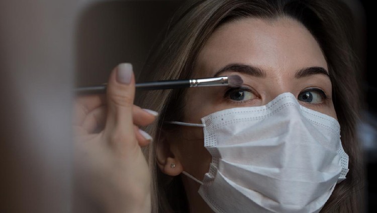 girl in medical mask against coronovirus does eye makeup. Covid-19. Covid-20. Young women make-up in beauty salon.