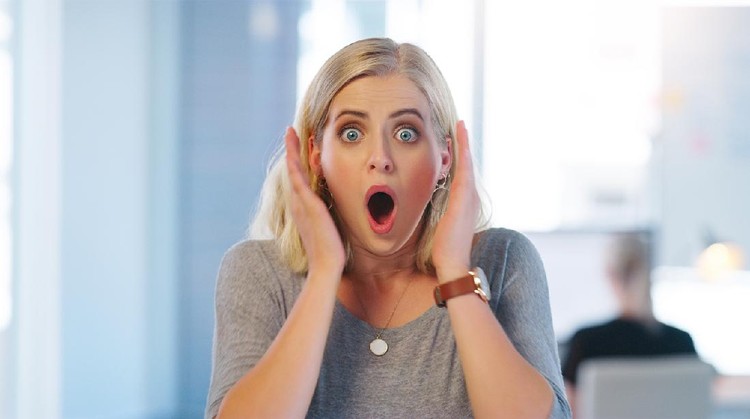 Portrait of a confident young businesswoman looking surprised and holding her hands close to her face inside of the office