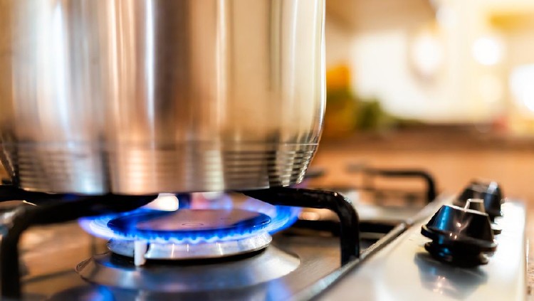 Macro closeup of modern luxury gas stove top with blue fire flame knobs and stainless steel pot with reflection and bokeh blurry blurred background