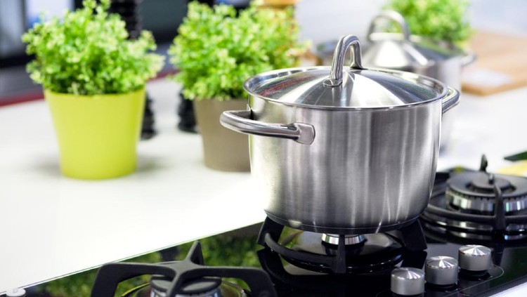 Macro closeup of modern luxury gas stove top with blue fire flame knobs and stainless steel pot with reflection and bokeh blurry blurred background