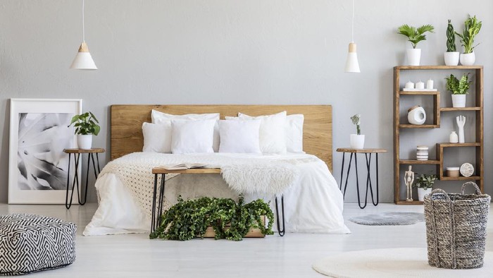 Patterned pouf and basket in bright bedroom interior with lamps, plants and poster next to bed. Real photo