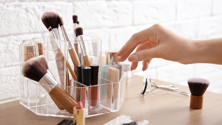 Woman taking lipstick from organizer for makeup cosmetic products on dressing table