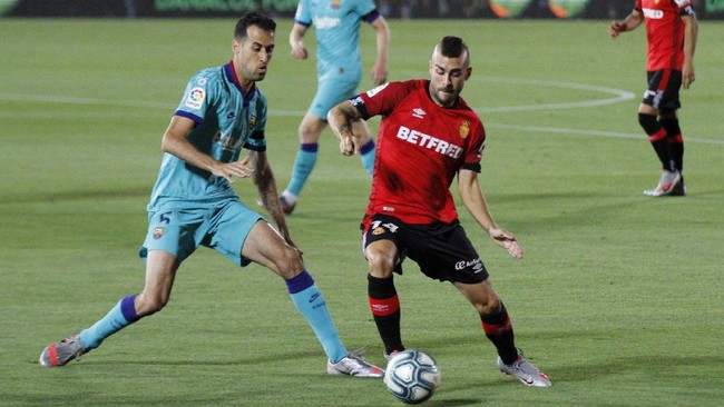 Barcelona's Sergio Busquets, left, vies for the ball with Mallorca's Dani Rodriguez during the Spanish La Liga soccer match between Mallorca and FC Barcelona at Son Moix Stadium in Palma de Mallorca, Spain, Saturday, June 13, 2020. With virtual crowds, daily matches and lots of testing for the coronavirus, soccer is coming back to Spain. The Spanish league resumes this week more than three months after it was suspended because of the COVID-19 pandemic. (AP Photo/Francisco Ubilla)