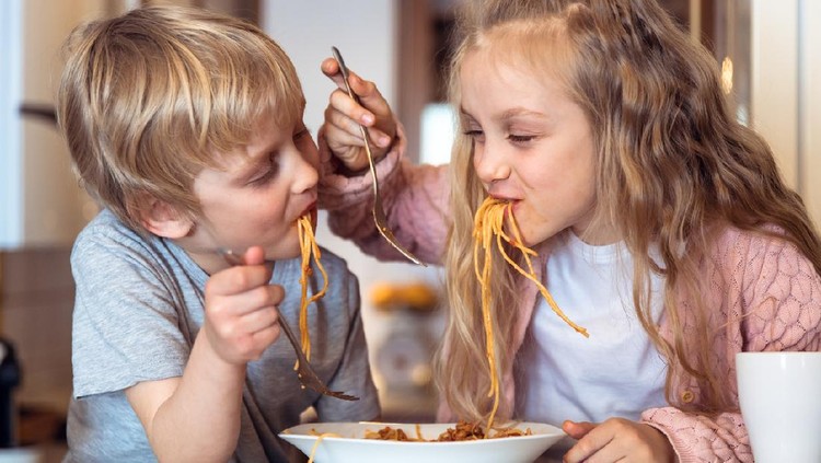 Cute children having fun while eating spaghetti with bolognese sauce at home