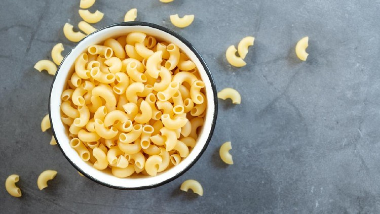 raw elbow macaroni in enamel bowl on dark cement table background.