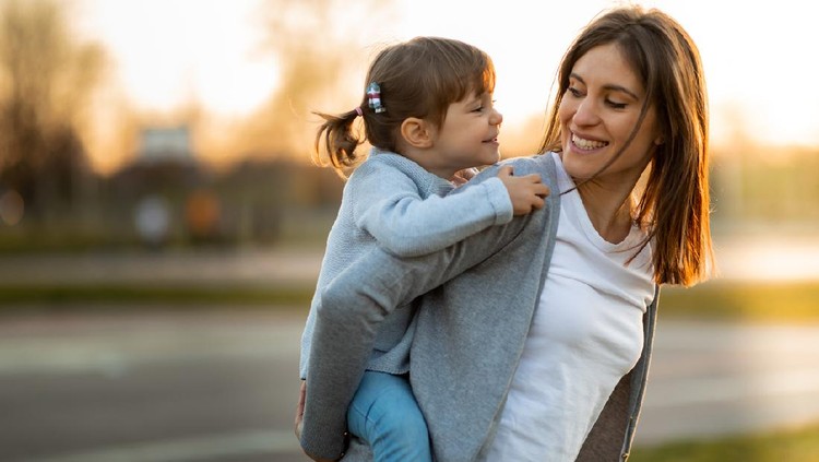 1138269305 Mother and little girl having fun in piggyback ride outdoors.