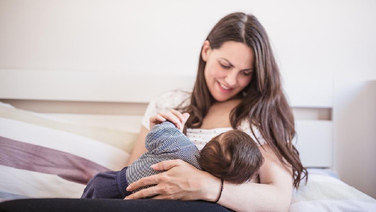 Ibu menyusui Young mother breastfeeding her baby boy in the bedroom. Belgrade, Serbia